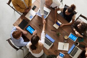 Top view of a diverse team collaborating in an office setting with laptops and tablets, promoting cooperation.