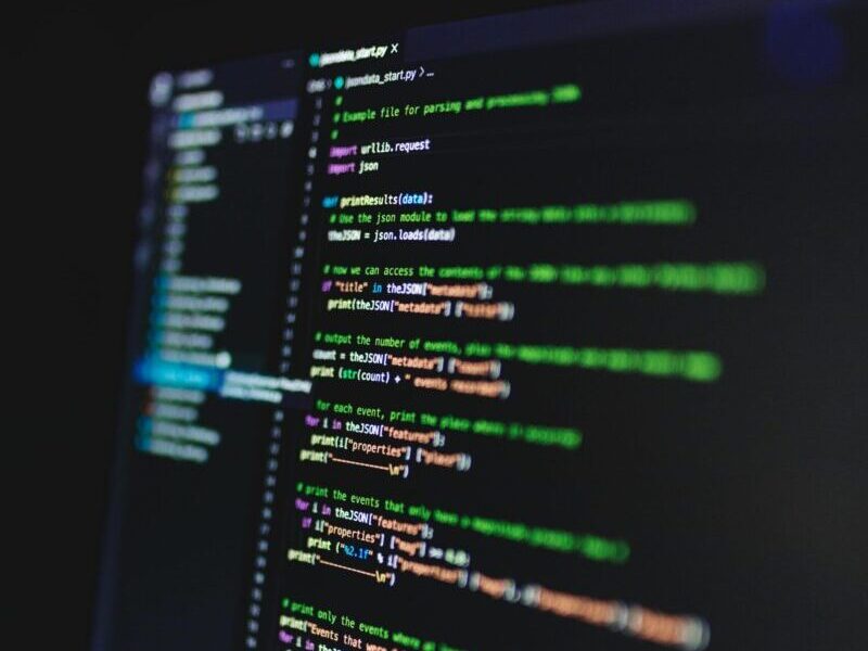 Vertical shot of colorful programming code on a screen in a dark room, highlighting technology work.