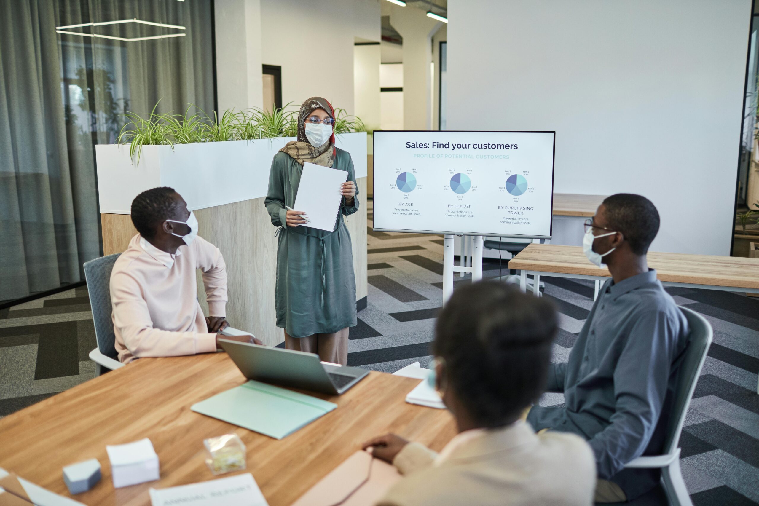 Colleagues wearing masks in a modern office discussing sales strategies.